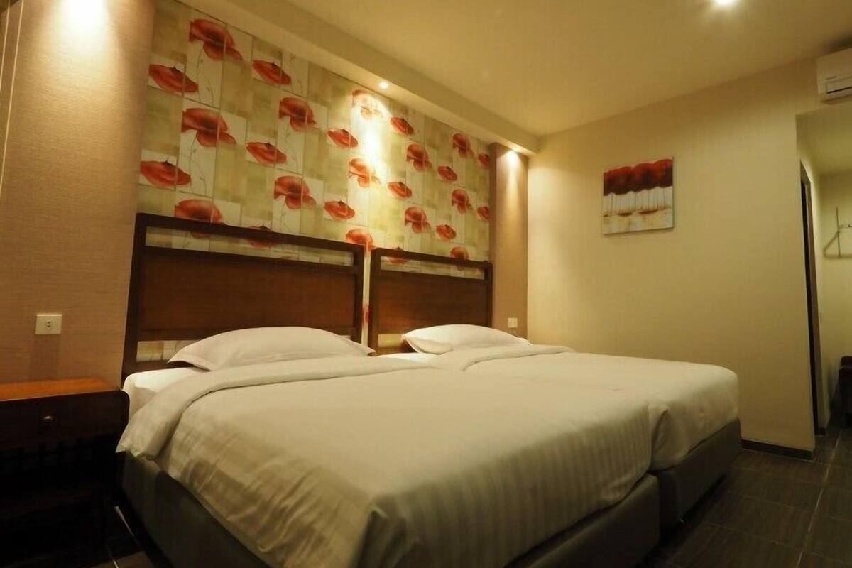 Habitación de hotel con dos camas, cabecera de madera, decoración floral en la pared y un pequeño cuadro.