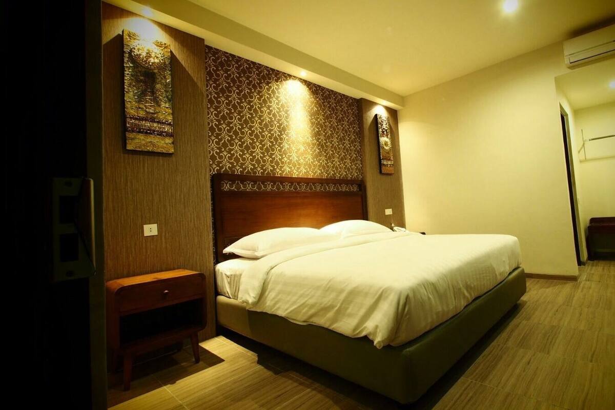 Una habitación de hotel con una cama, una mesita de noche de madera, un escritorio y un espejo.