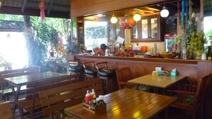 A restaurant with wooden furniture, a counter with various items, and a view of greenery outside. - Safe House Court (Chiang Mai)