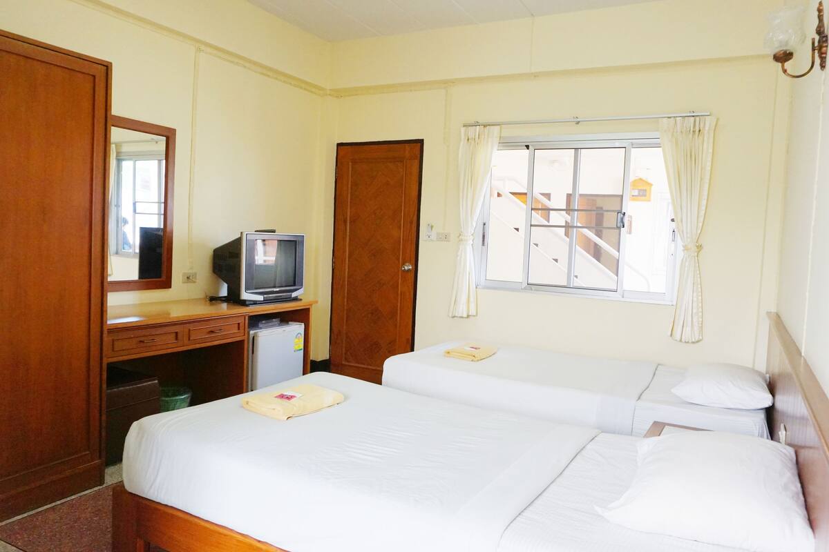 A hotel room with two beds, a desk with a television, a wardrobe, and a window with curtains.
