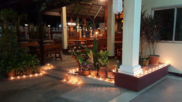 An outdoor seating area with wooden benches and potted plants, surrounded by a low wall of candles. - Safe House Court (Chiang Mai)