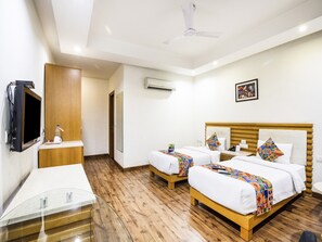 A hotel room with two beds, a TV, a desk, and a glass table.
