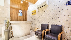 Una zona de recepción con un mostrador de madera, dos sillones de cuero, un reloj y una pared de mosaicos.