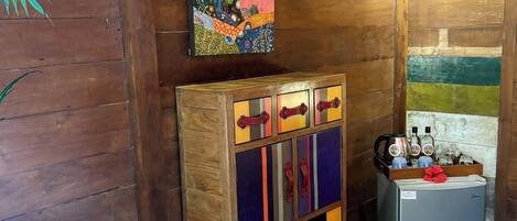 A wooden cabin interior with a colorful cabinet, a refrigerator, and a painting on the wall.