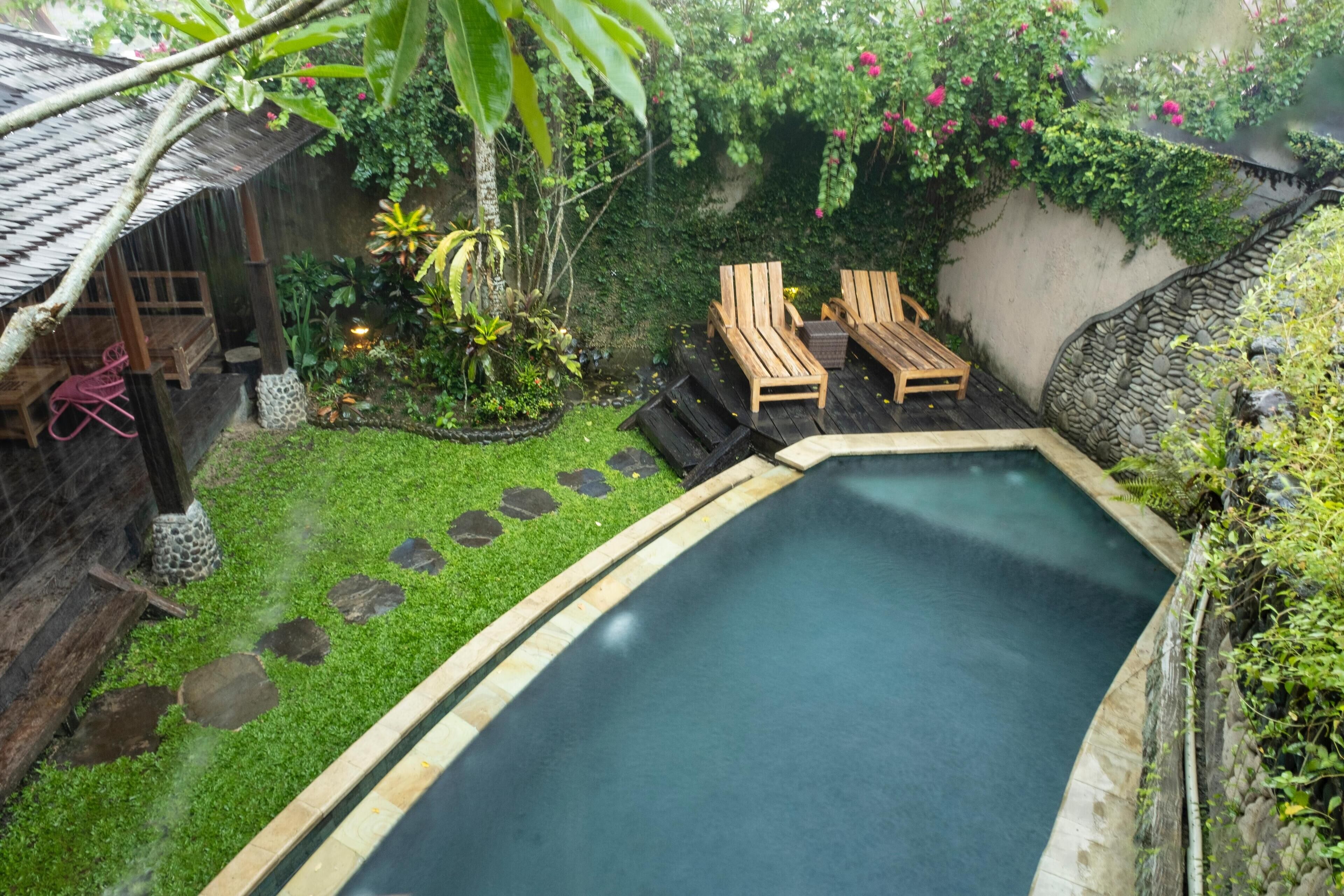 Ein Poolbereich mit Holzterrasse, zwei Liegestühlen und einem kleinen Garten mit Pflanzen und einem Kiesweg.
