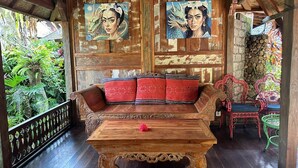 A wooden bench with red cushions, a wooden table, and two framed paintings on the wall. - Bali Bohemia (Ubud)