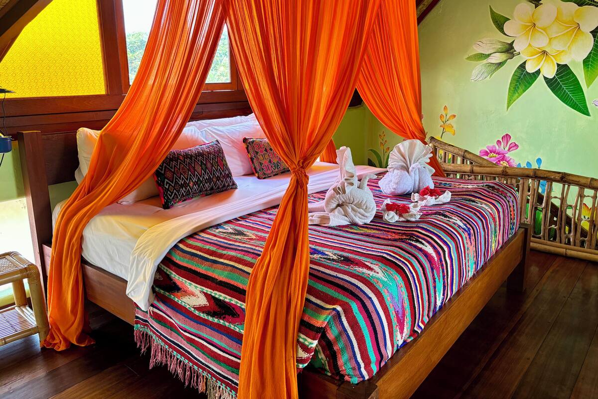 A bed with an orange canopy, colorful pillows, and a striped blanket.