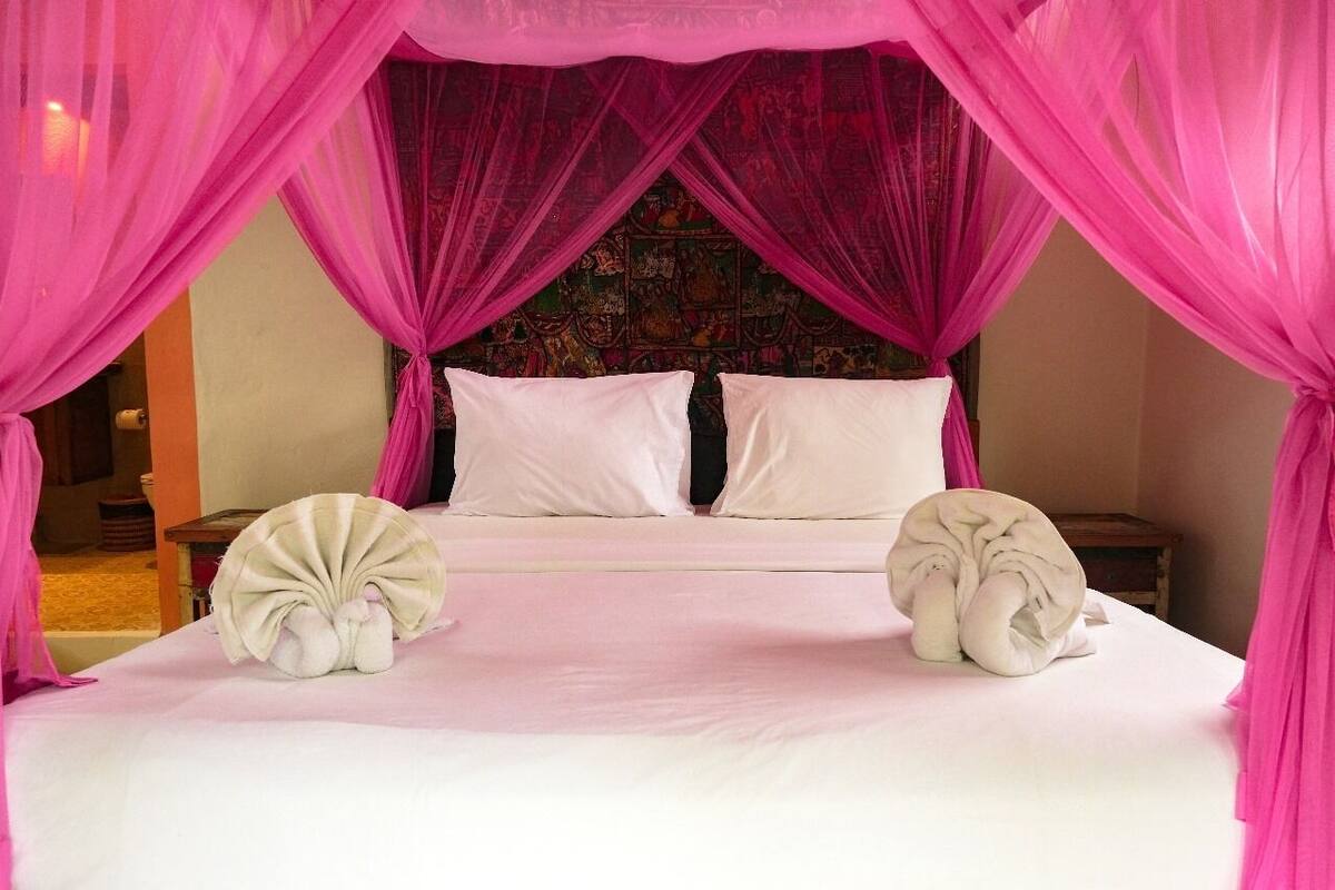 A bed with pink curtains, white pillows, and a decorative headboard.