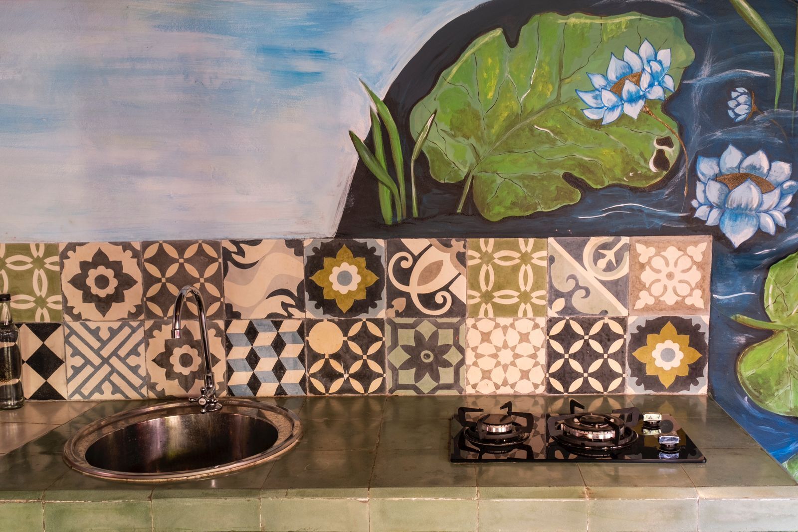 Una cocina con un lavamanos, dos estufas a gas y un salpicadero decorativo con motivos florales.