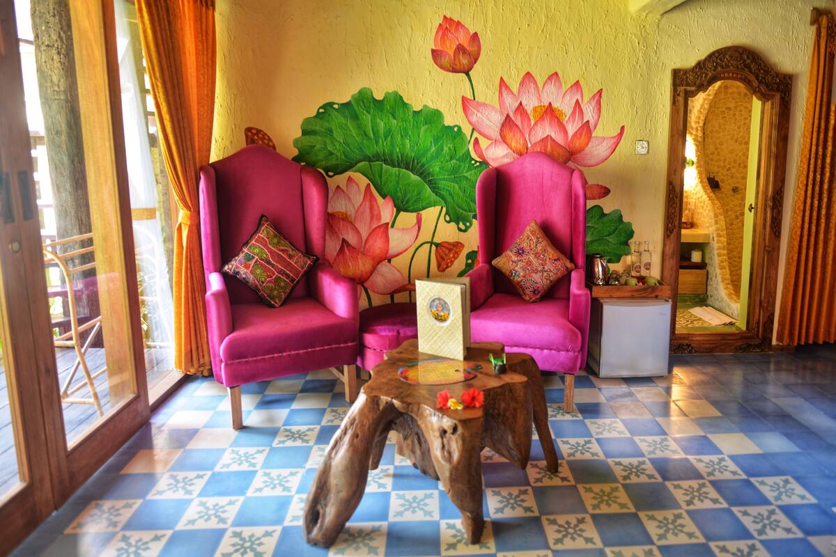 A room with two pink armchairs, a small wooden table, and a large lotus mural on the wall.