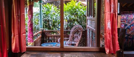 Un banco de madera con vista a un jardín a través de una ventana con cortinas rojas.