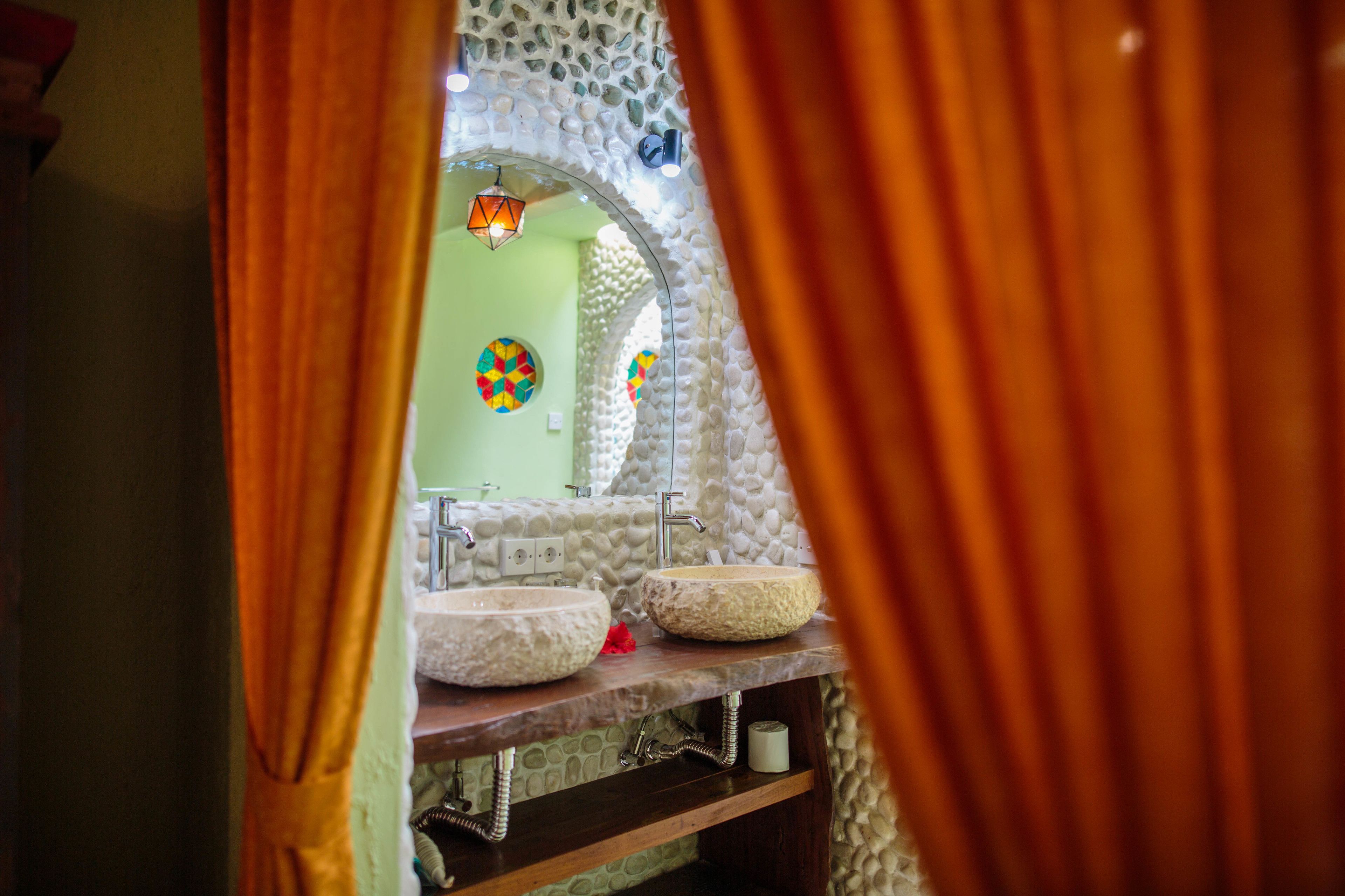 A bathroom with two stone sinks, a mirror, and a colorful wall decoration.