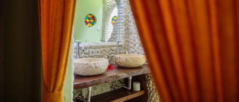 A bathroom with two stone sinks, a mirror, and a colorful wall decoration.