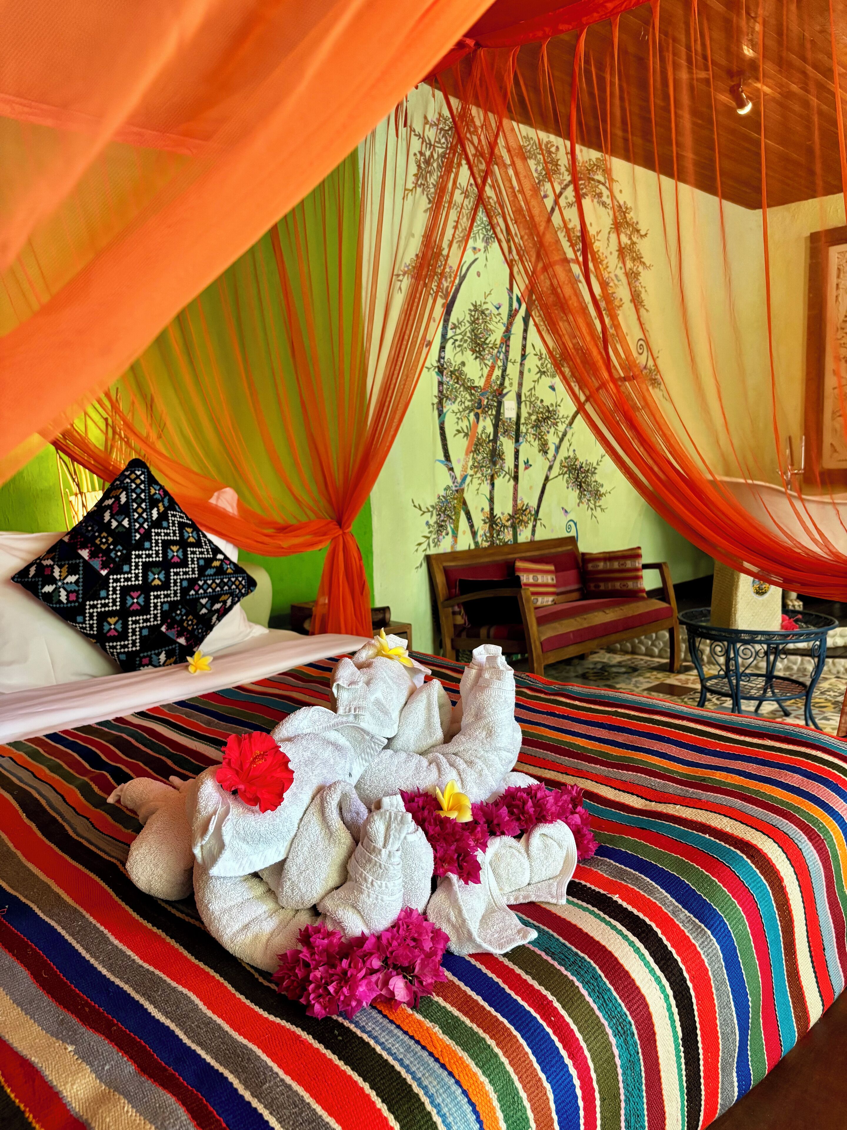 A bed with a colorful striped bedspread, a red flower, and a white towel arrangement.