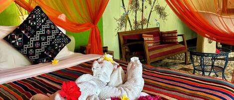 A bed with a colorful striped bedspread, a red flower, and a white towel arrangement.