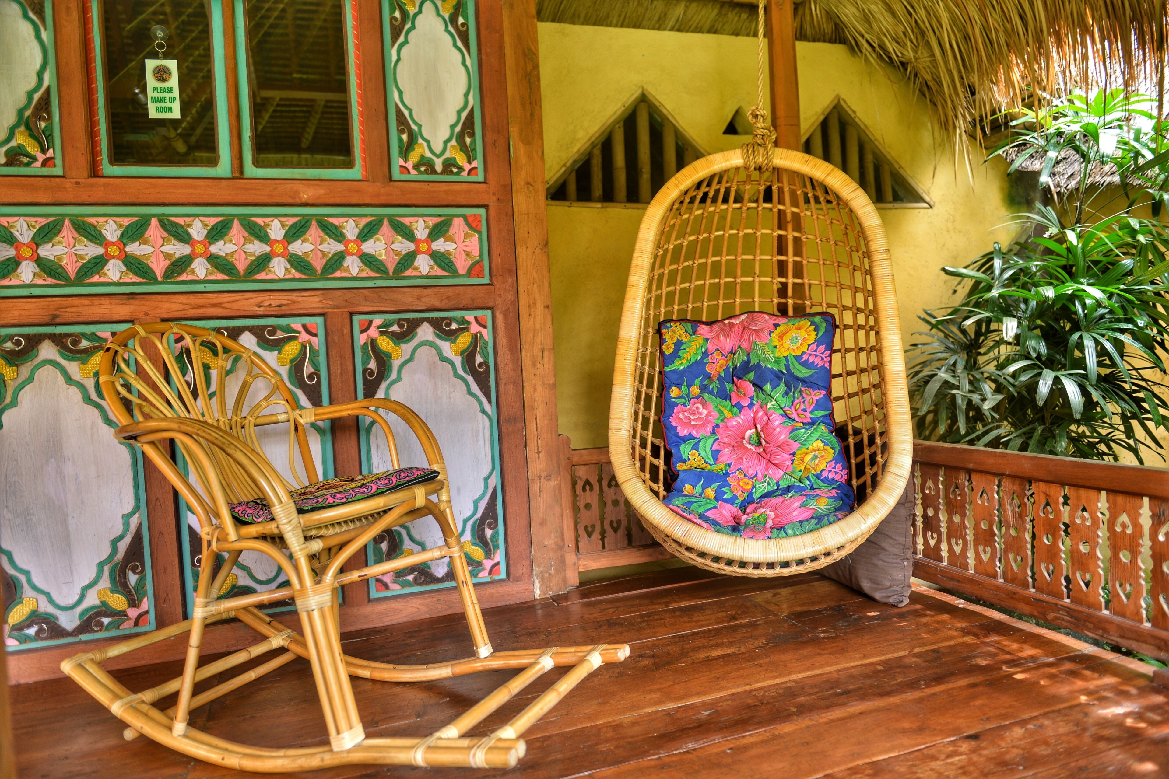 Un fauteuil à bascule en osier, agrémenté d’un coussin à motifs floraux, sur une véranda en bois.