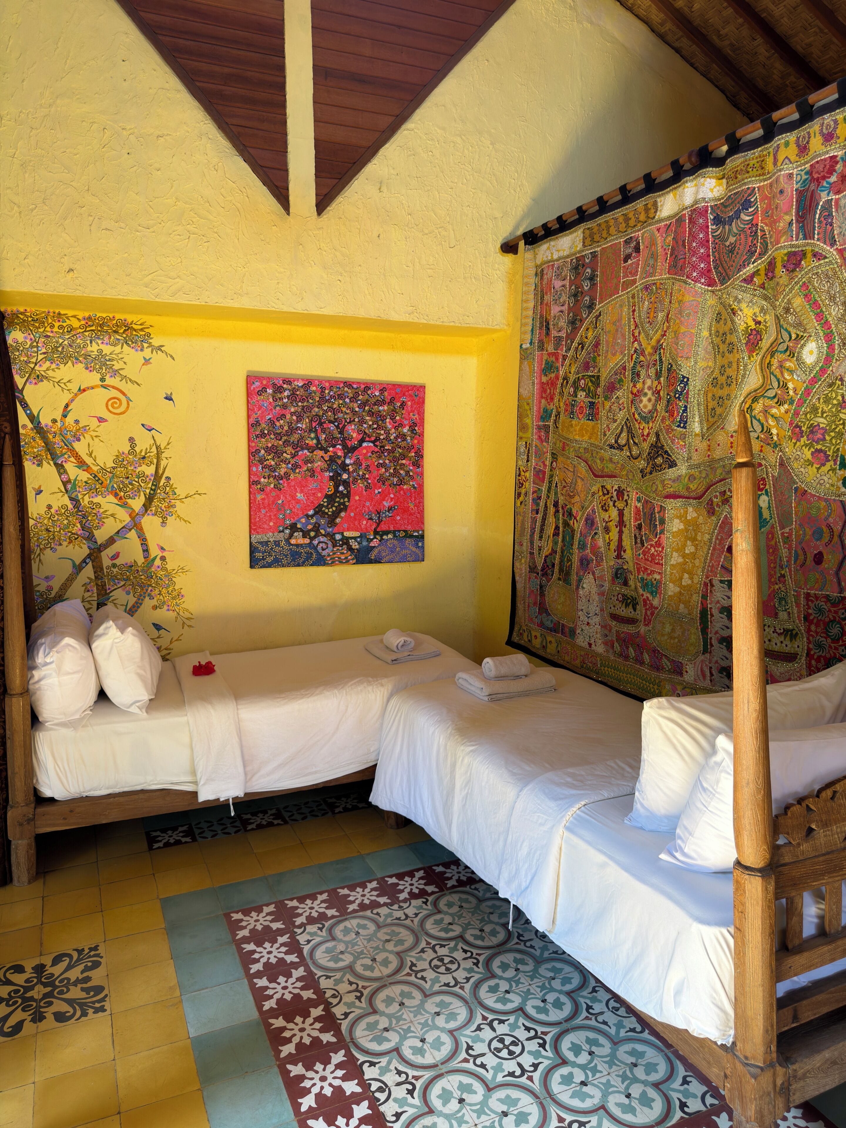 Une chambre avec deux lits, un plafond en bois, une tapisserie colorée et un sol à motifs.