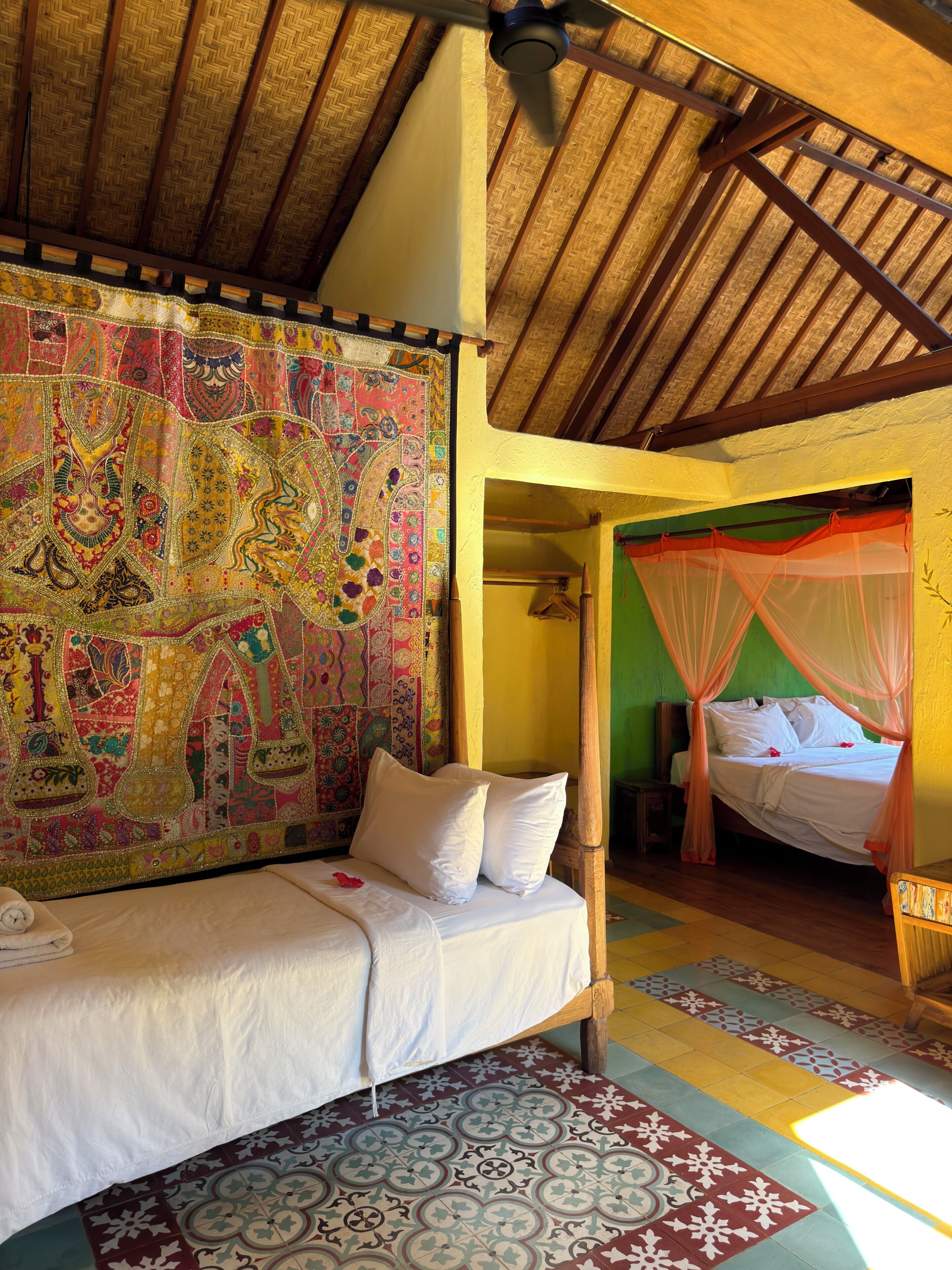 A room with a bed, a canopy bed, a colorful tapestry, and a patterned floor.