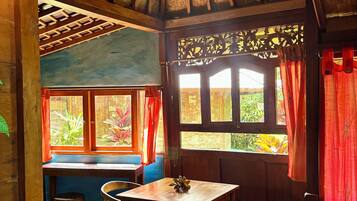 Un interior rústico de madera con una mesa y sillas, ventanas grandes con cortinas y una lámpara decorativa en el techo.