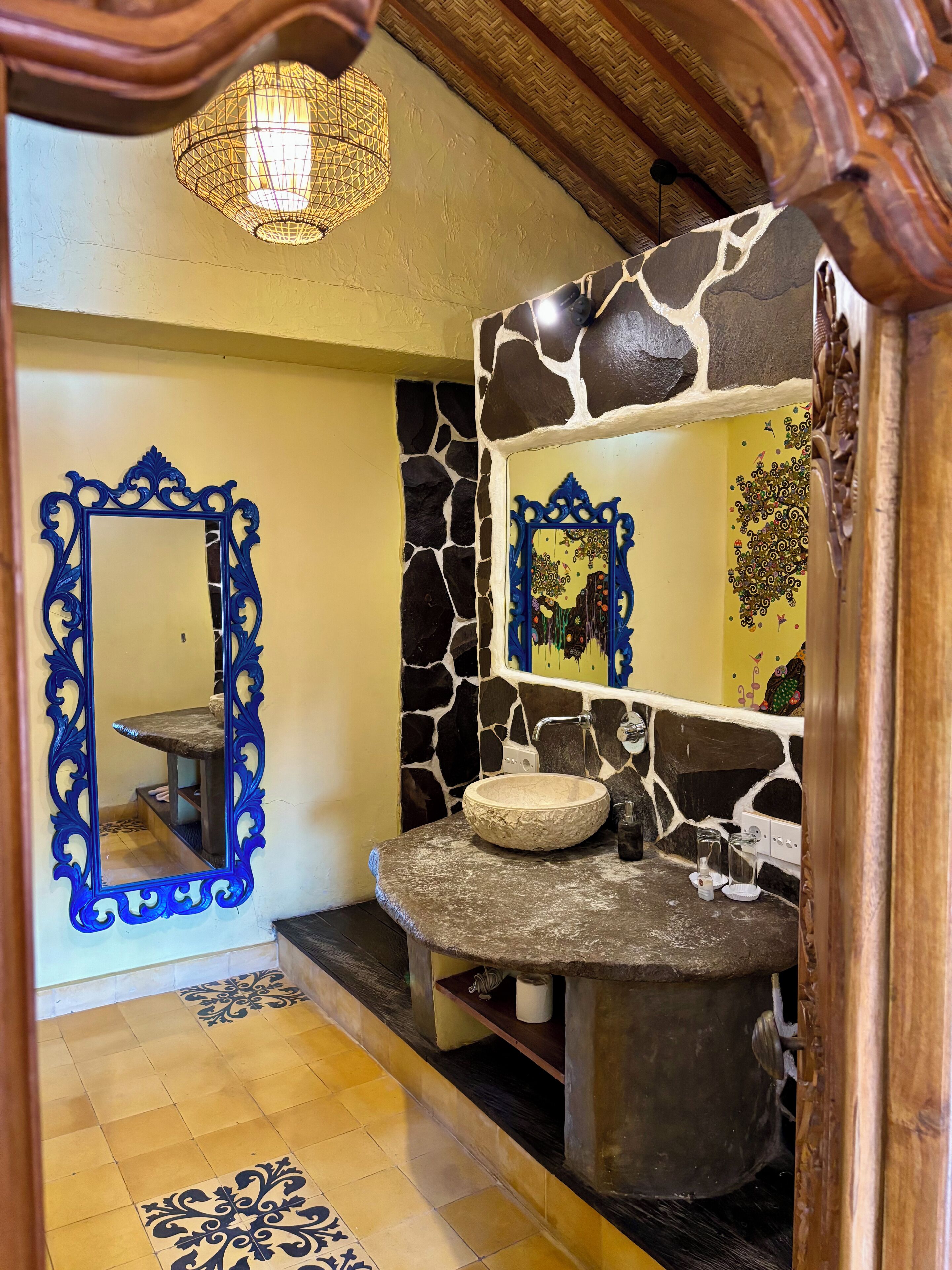 A bathroom with a stone sink, a blue ornate mirror, and a decorative wall.