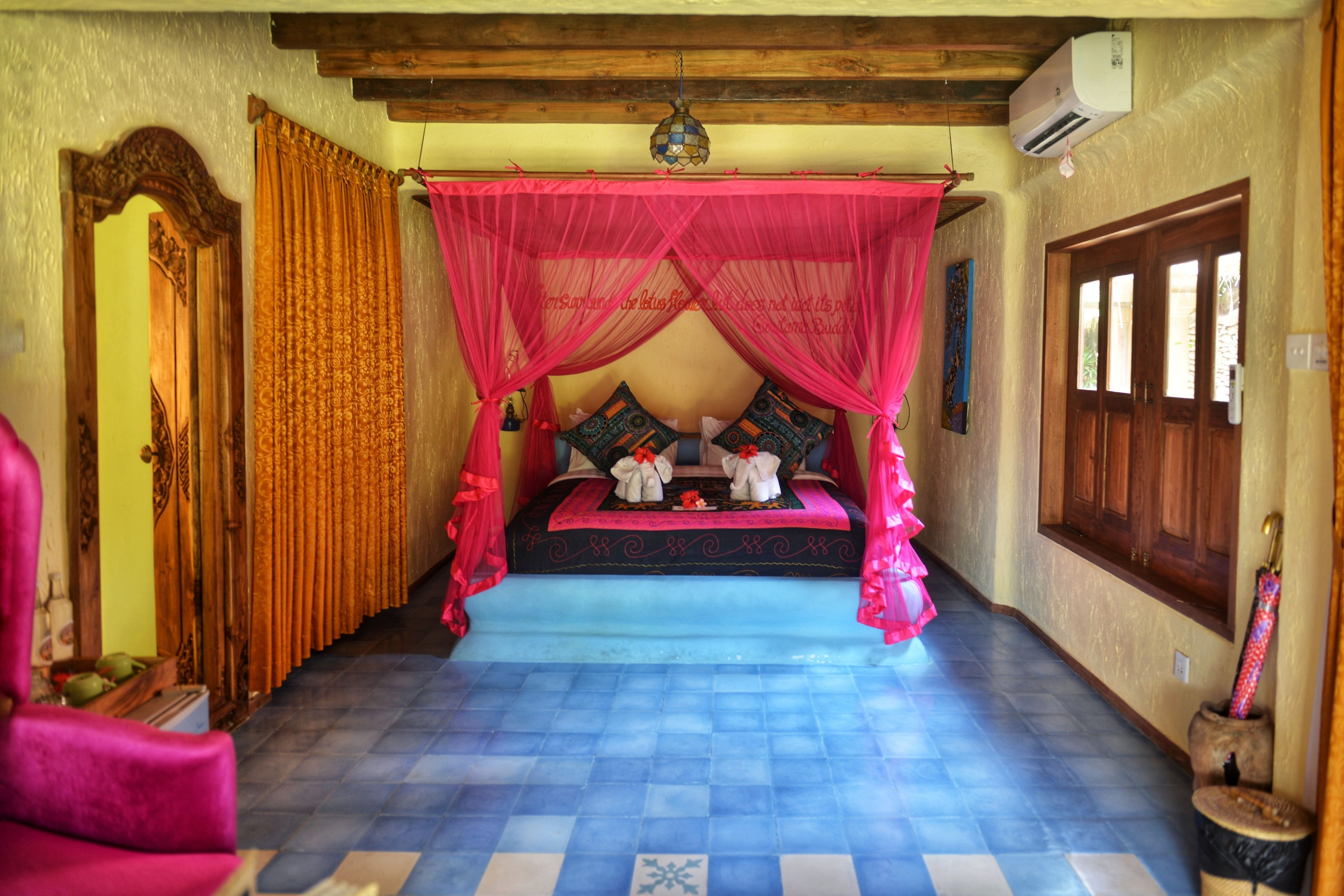 Un dormitorio con una cama bajo un dosel rosa, una puerta de madera y una ventana con vistas.