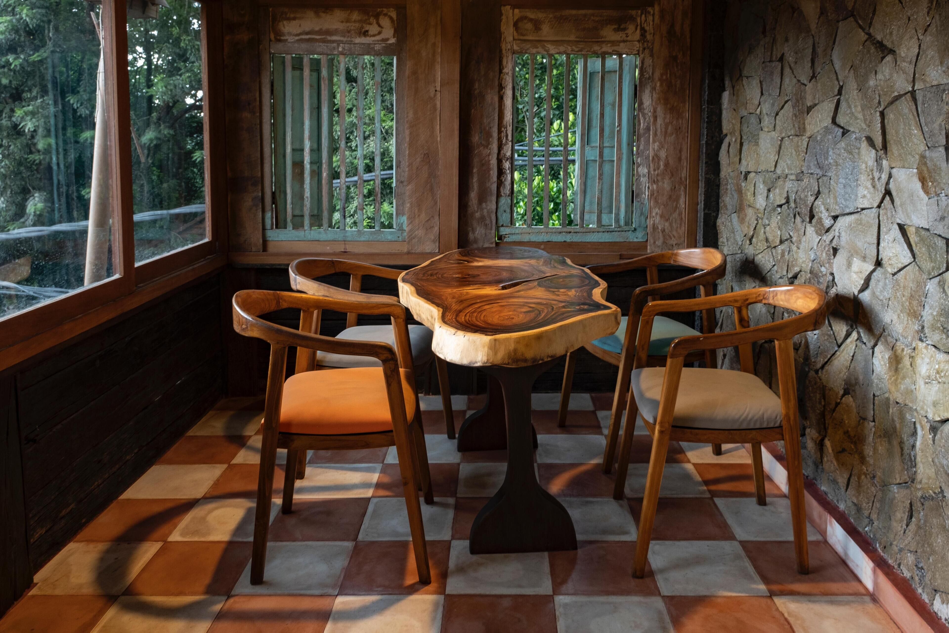 A dining area with a wooden table and chairs, large windows with bars, and a stone wall.
