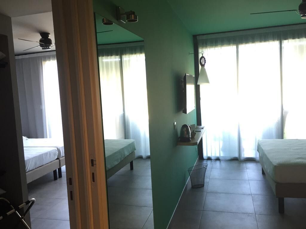 Een hotelkamer met twee eenpersoonsbedden, een bureau met lamp, een plafondventilator en een groot raam met gordijnen.