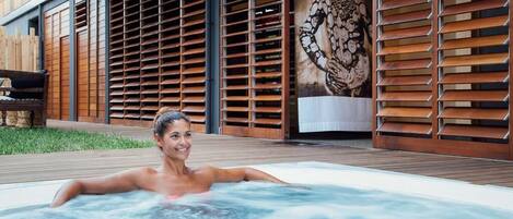 A person relaxing in a hot tub with a wooden deck and a large mural in the background.