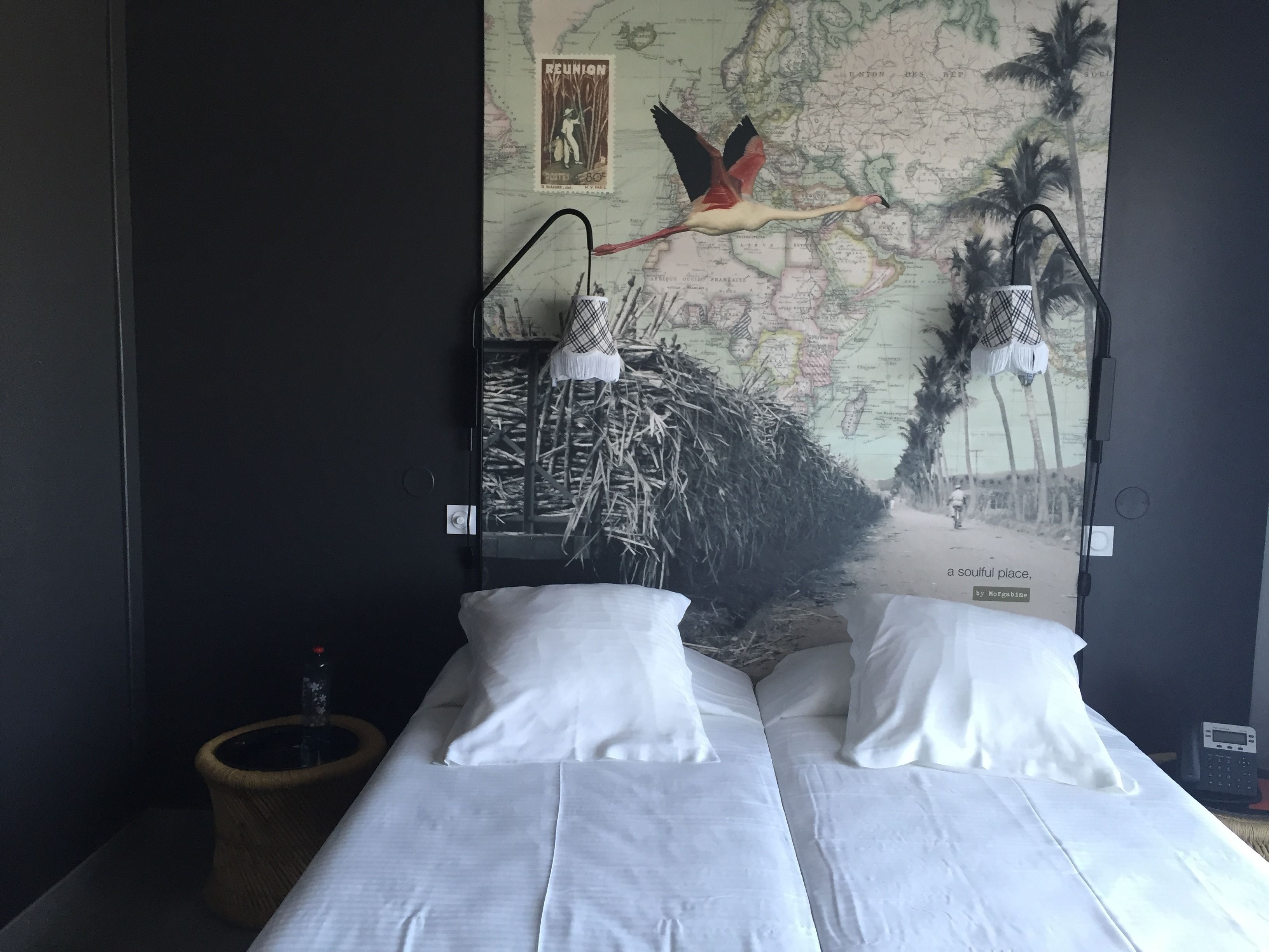 A hotel room with two beds, a map on the wall, a telephone, and a small trash bin.