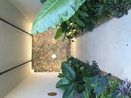 Un patio con un muro de piedra, plantas verdes grandes y una barandilla de metal.