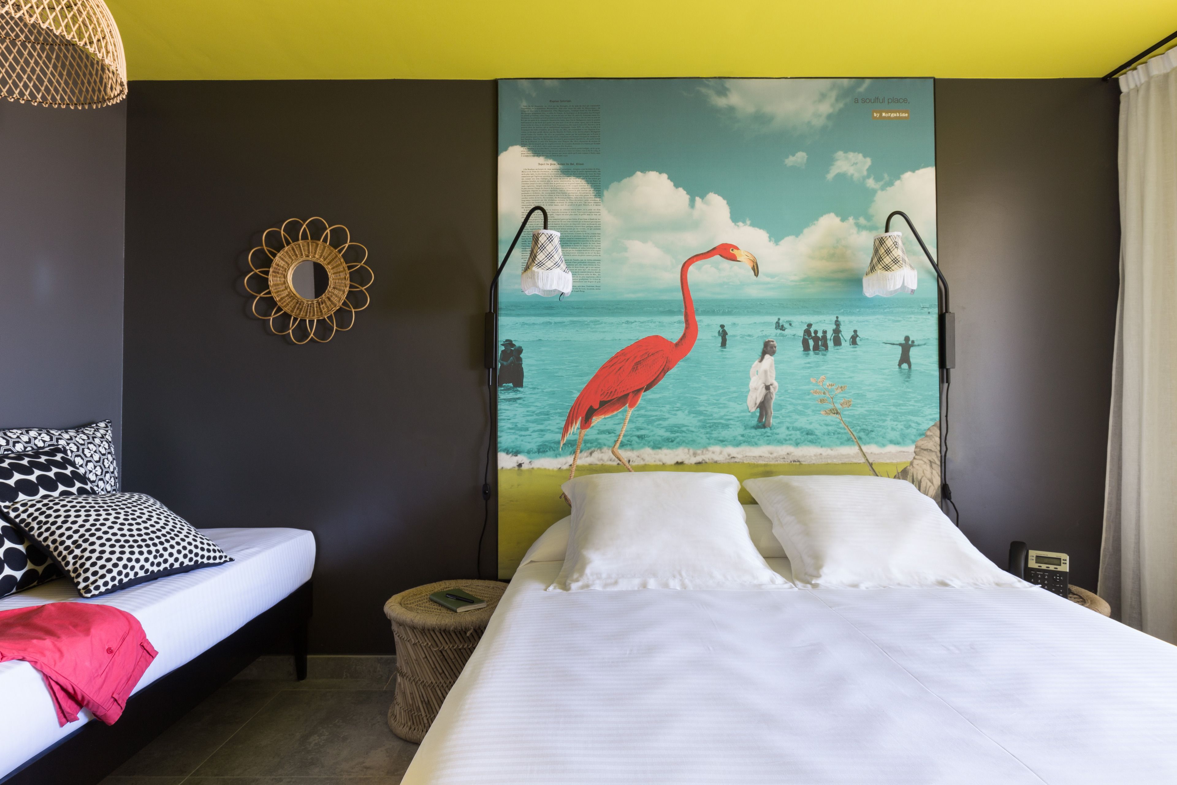 A hotel room with a bed, a wall-mounted lamp, a decorative mirror, and a mural of a beach scene.