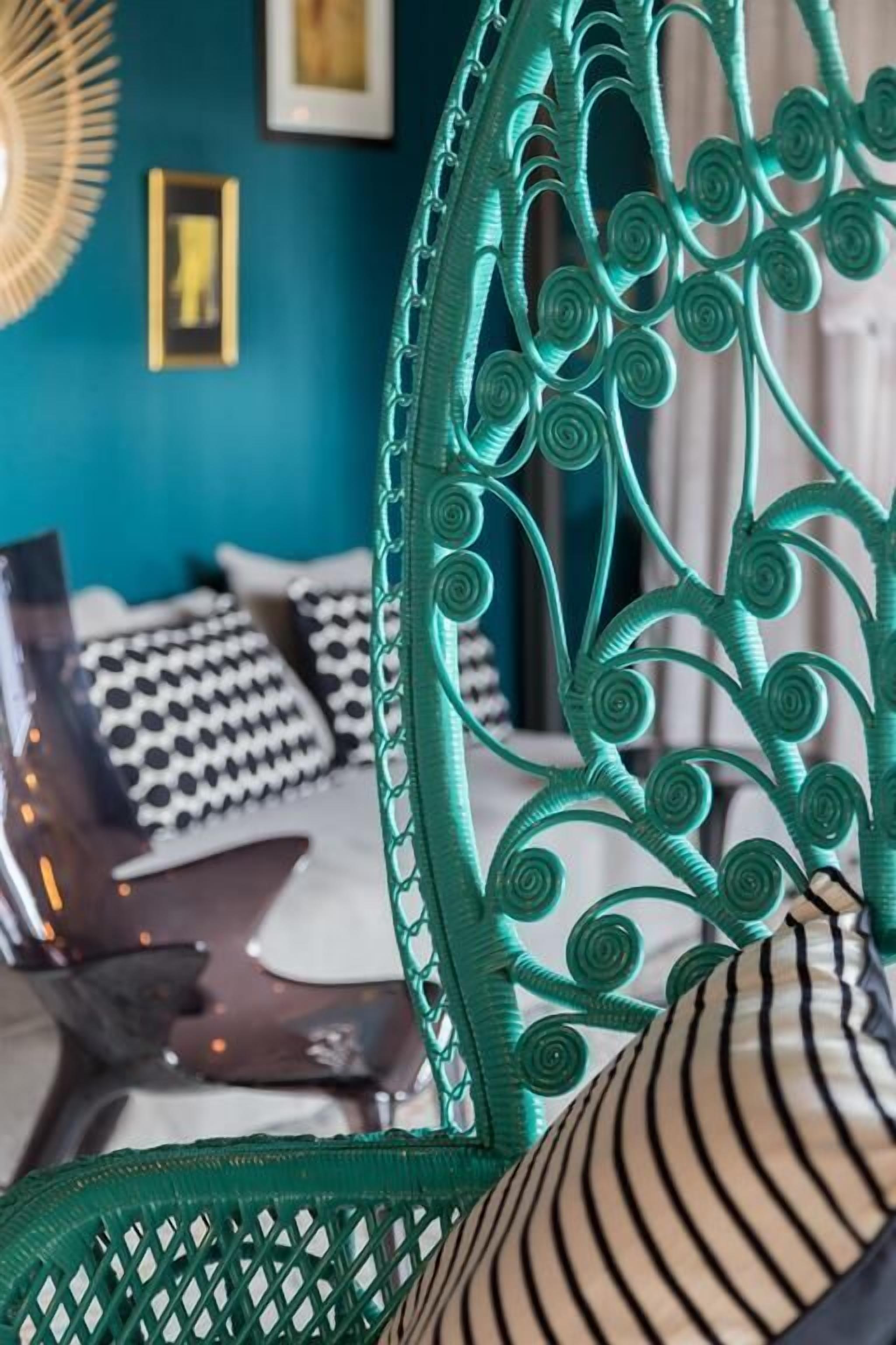 A teal-colored chair with intricate spiral designs, a bed with patterned pillows, and a laptop on the bed.