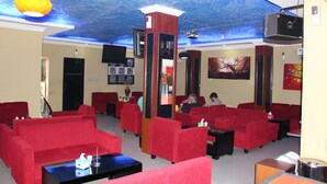 A hotel lobby with red sofas, a black coffee table, and a ceiling with a blue water-like design. - Hollywood Hotel (Jakarta)