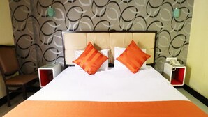 A hotel room with a bed, two orange pillows, a nightstand, a chair, and a patterned wallpaper. - Hollywood Hotel (Jakarta)