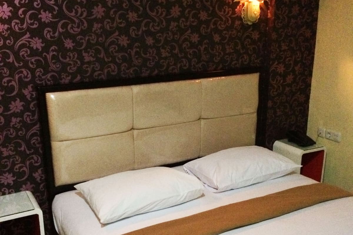Une chambre d’hôtel avec un lit, une table de chevet et une lampe fixée au mur.