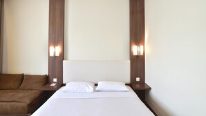 A hotel room with a bed, two bedside tables, a brown sofa, and wall-mounted lights.