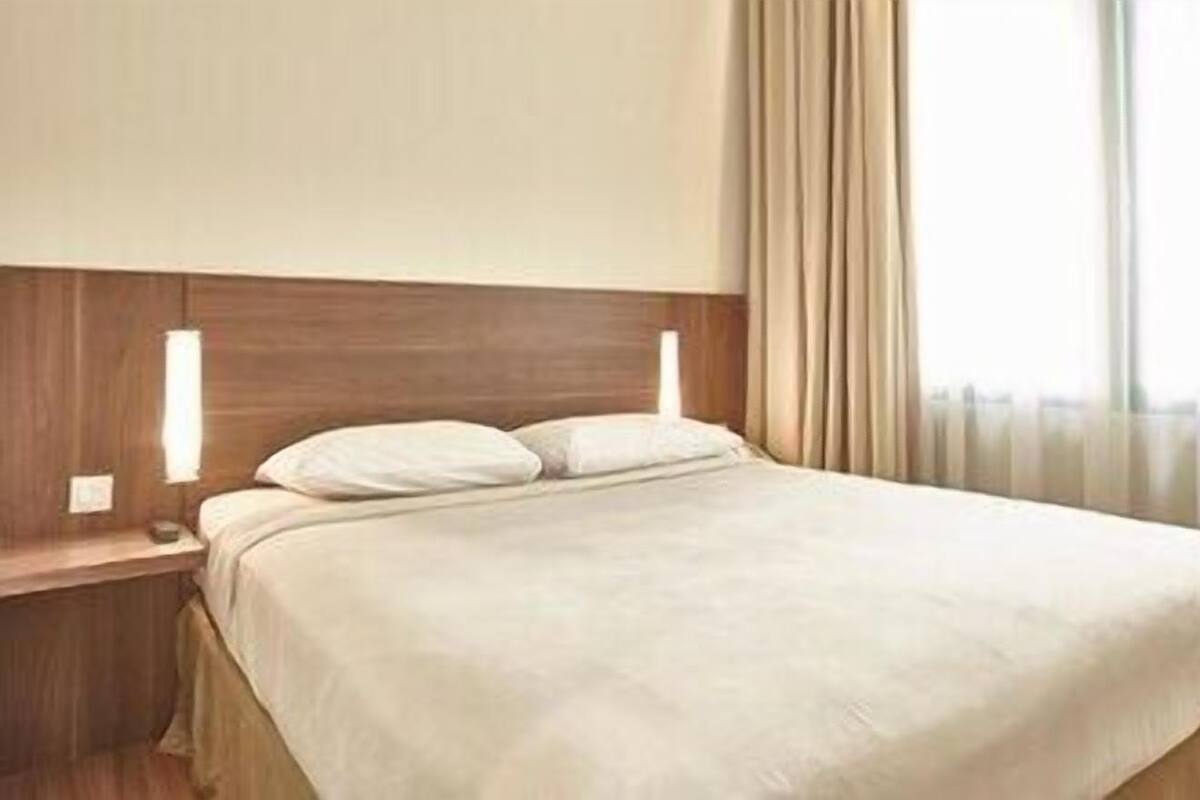 A hotel room with a bed, a nightstand, and a window with curtains.