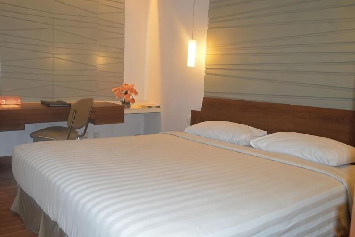 Une chambre d’hôtel avec un lit, un bureau et une chaise, ainsi qu’une lampe fixée au mur.