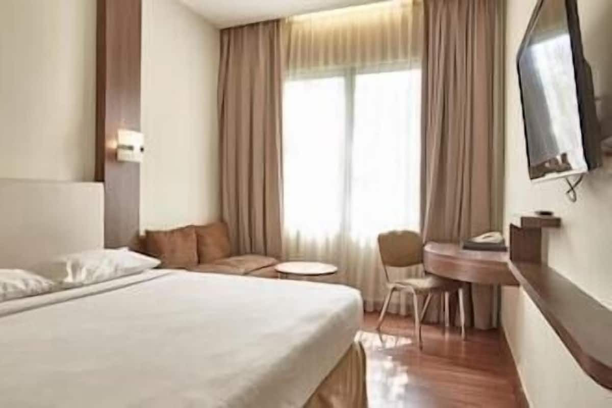 Une chambre d’hôtel avec un lit, une petite table ronde, une chaise et un téléviseur fixé au mur.