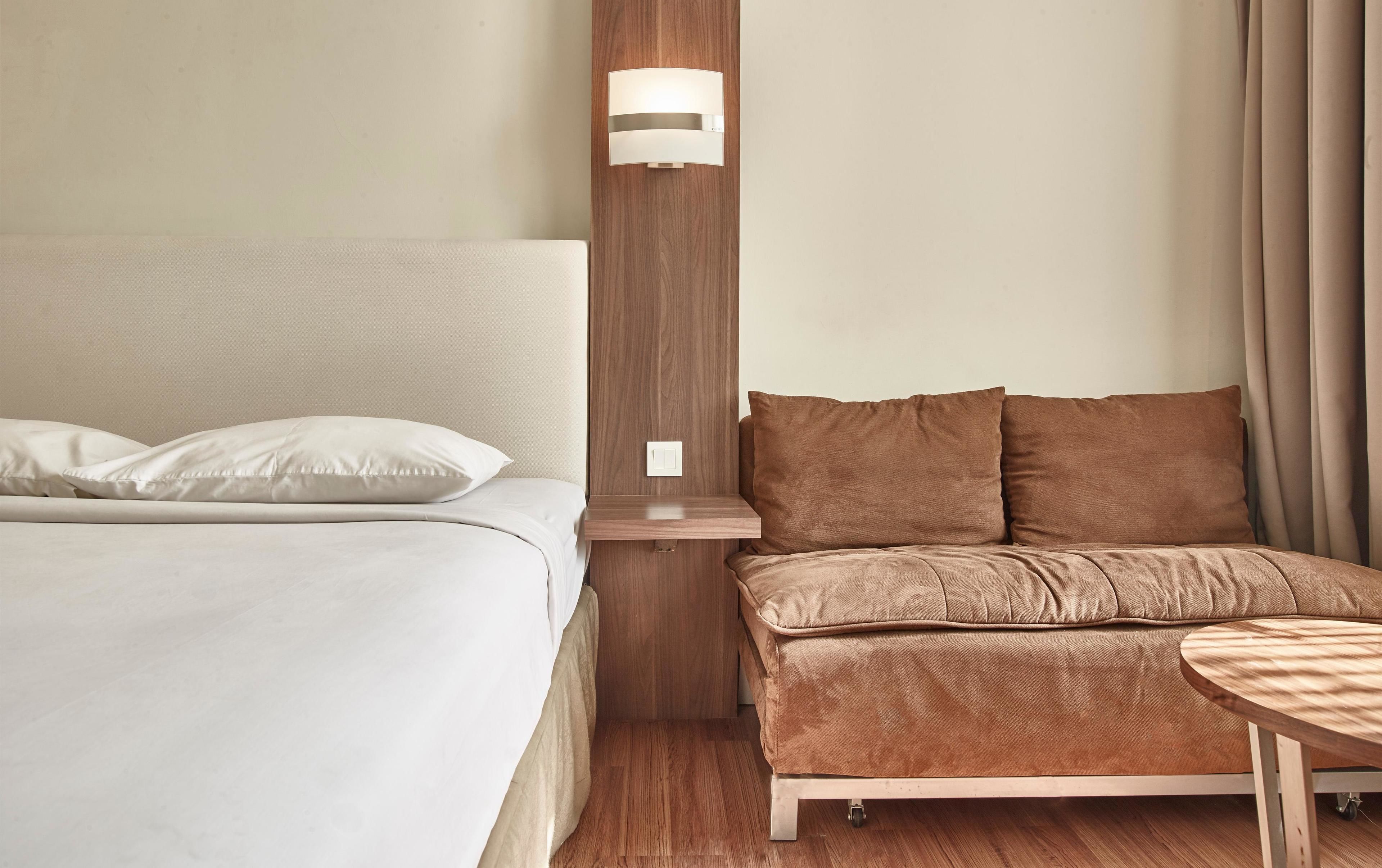 Una habitación de hotel con cama, sofá, una mesita y una lámpara fijada a la pared.