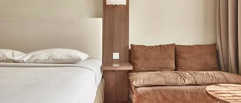 Una habitación de hotel con cama, sofá, una mesita y una lámpara fijada a la pared.
