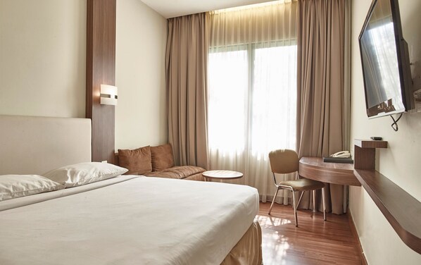 Une chambre d’hôtel avec un grand lit, un bureau avec une chaise, une télévision et une fenêtre avec des rideaux.