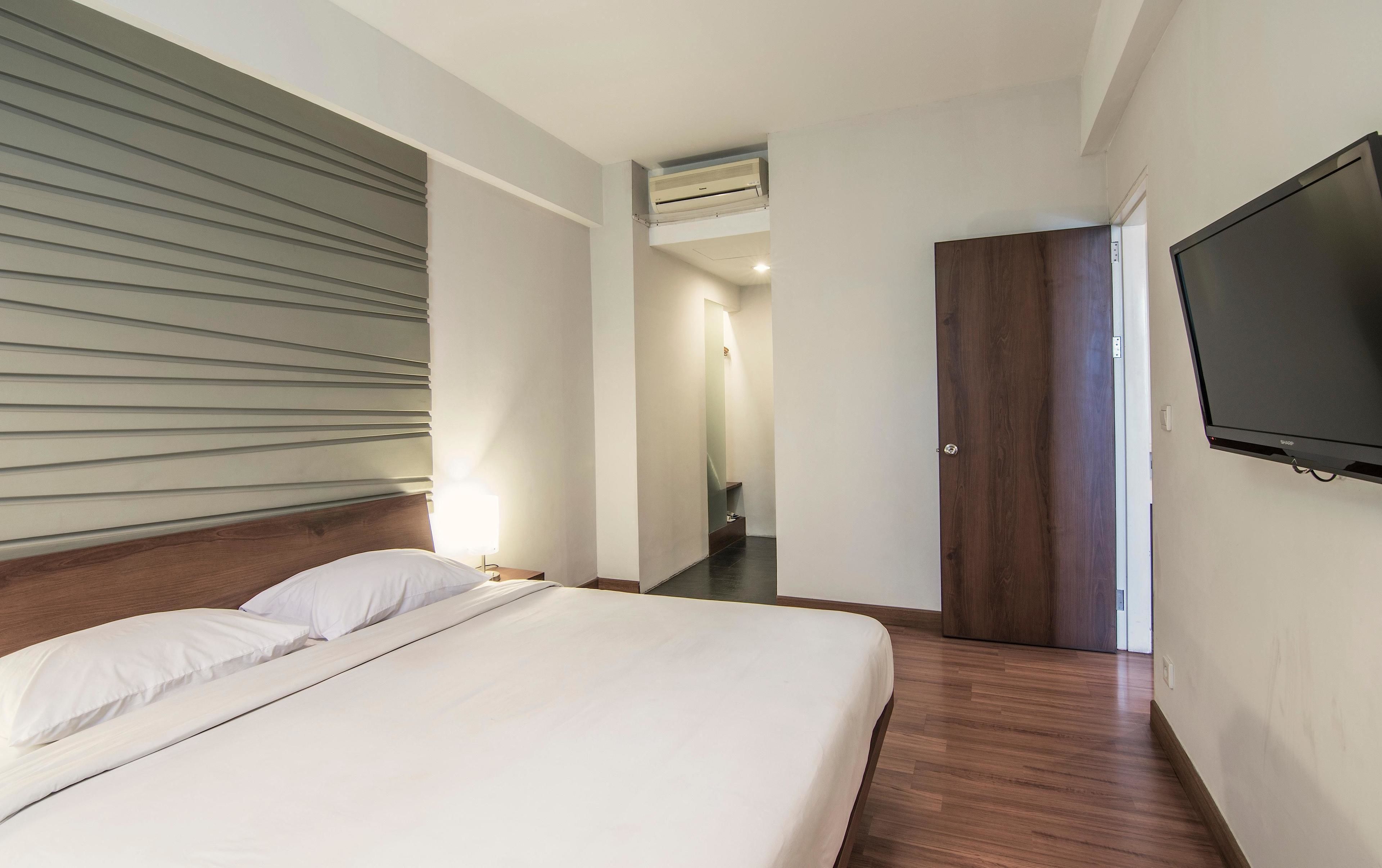 Une chambre d’hôtel avec un lit, un téléviseur fixé au mur et une porte en bois.