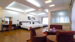 Ein Hotelzimmer mit zwei Betten, einem Essbereich mit Tisch und Stühlen, einem großen Fenster mit Blick auf Bäume und einer Decke mit Einbauleuchten.