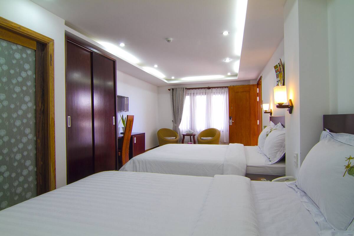 A hotel room with two beds, a desk, two chairs, a TV, and a window with curtains.