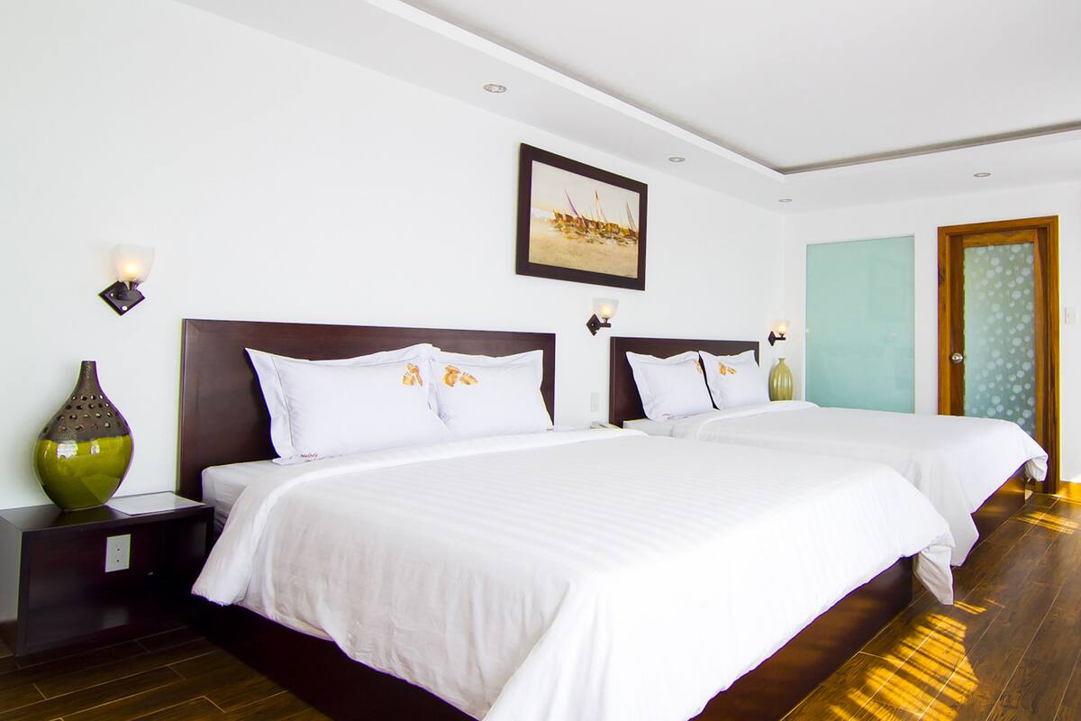 A hotel room with two beds, a painting on the wall, and a vase on the nightstand.