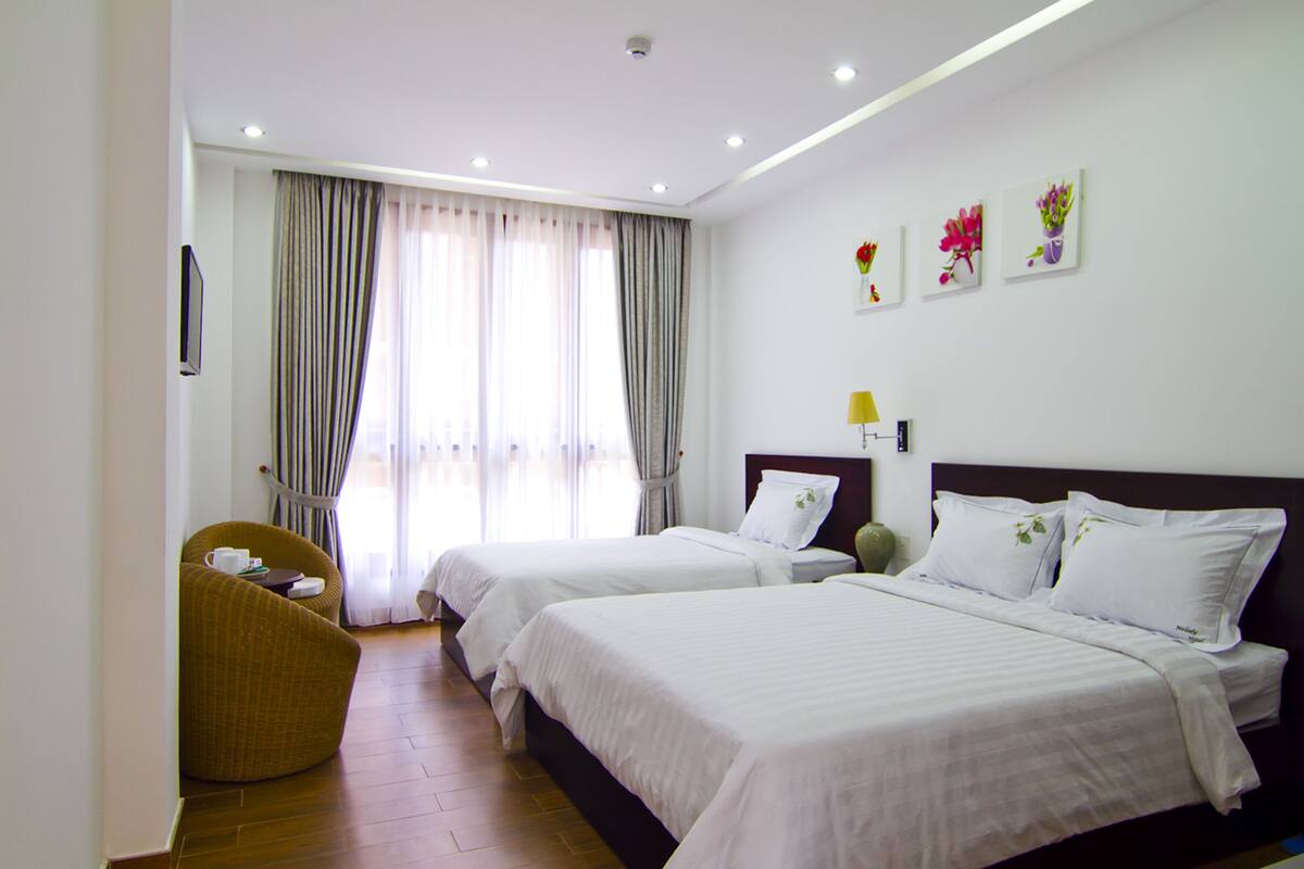 A hotel room with two beds, a sofa, and a large window with curtains.