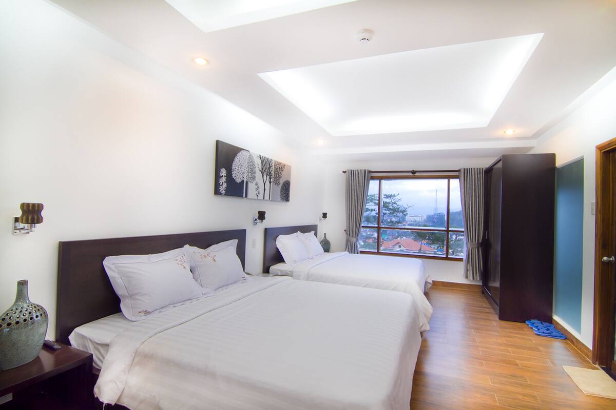 A hotel room with two beds, a skylight, a painting on the wall, and a view of the outside.