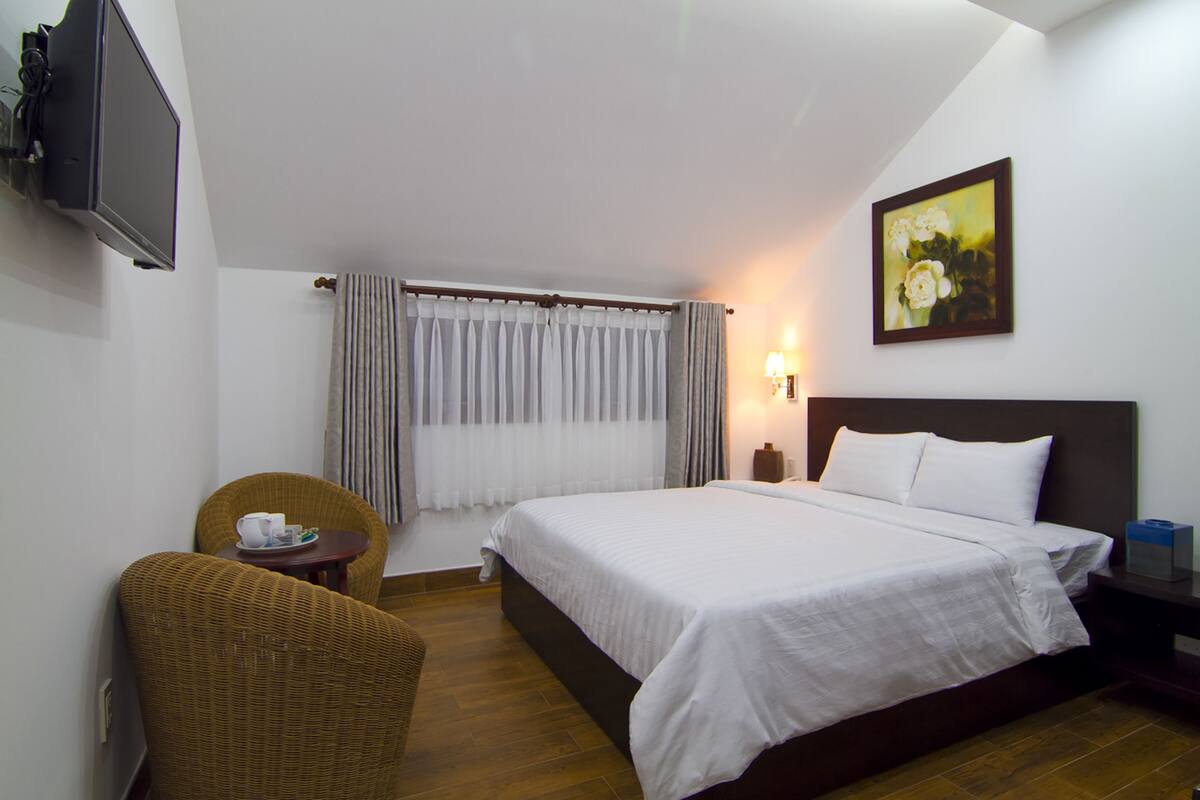 A hotel room with a bed, a television, a painting, a chair, and a small table.
