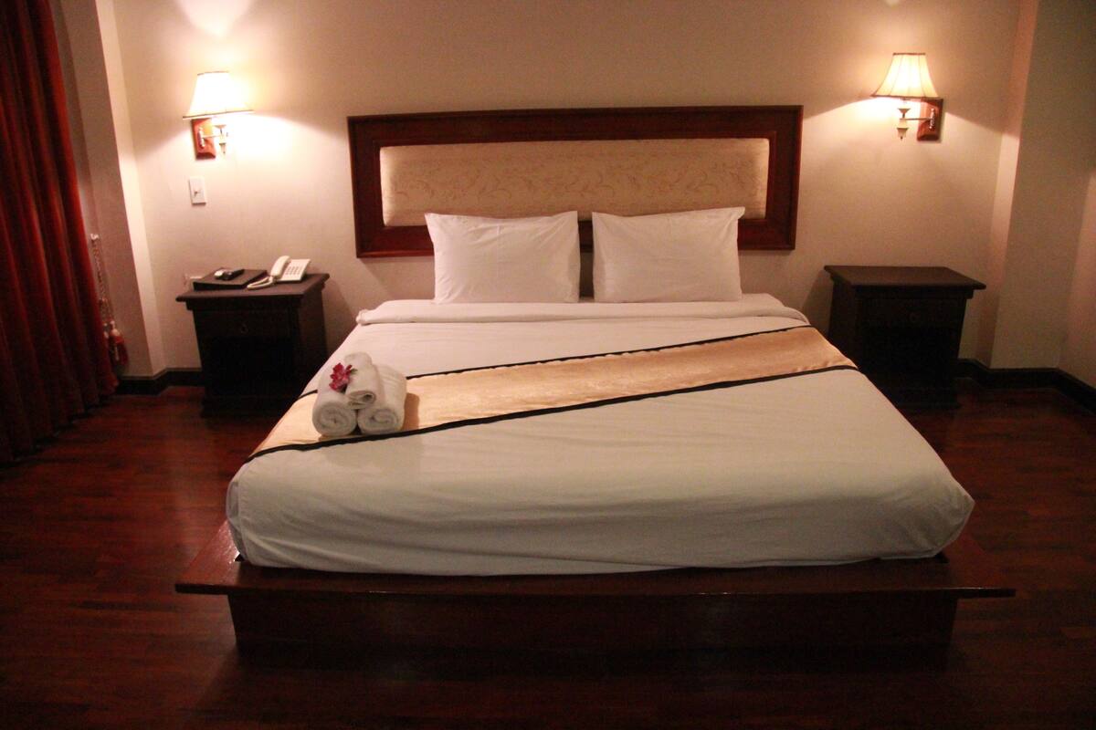 A hotel room with a large bed, two bedside tables, and two wall-mounted lamps.